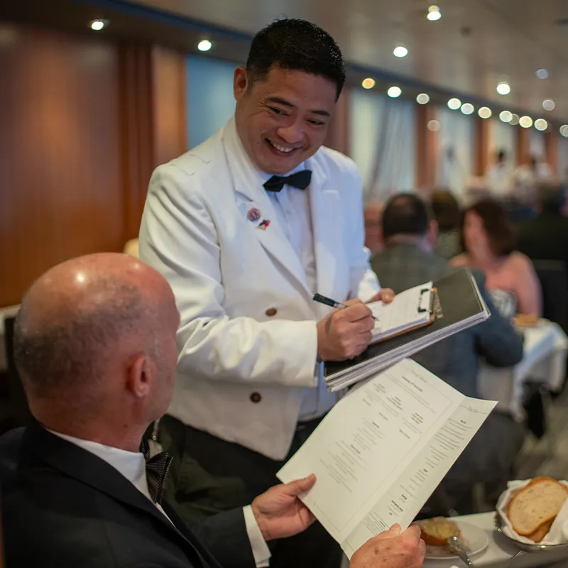 Smiling waiter in a white jacket takes an order from a man in Buckingham Restaurant