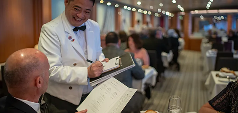 The waiter takes an order from a seated customer in BUCKINGHAM restaurant.