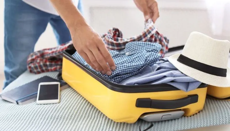 Person packing a yellow suitcase with clothes