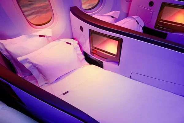 Virgin Atlantic airplane cabin with lie-flat seats in Upper Classes, white bedding, and ambient pink lighting.